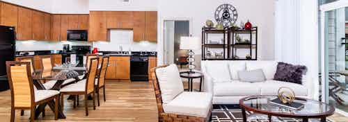 Interior view of a living room and kitchen at AMLI Park Avenue apartments with a dining room table and a plush white couch