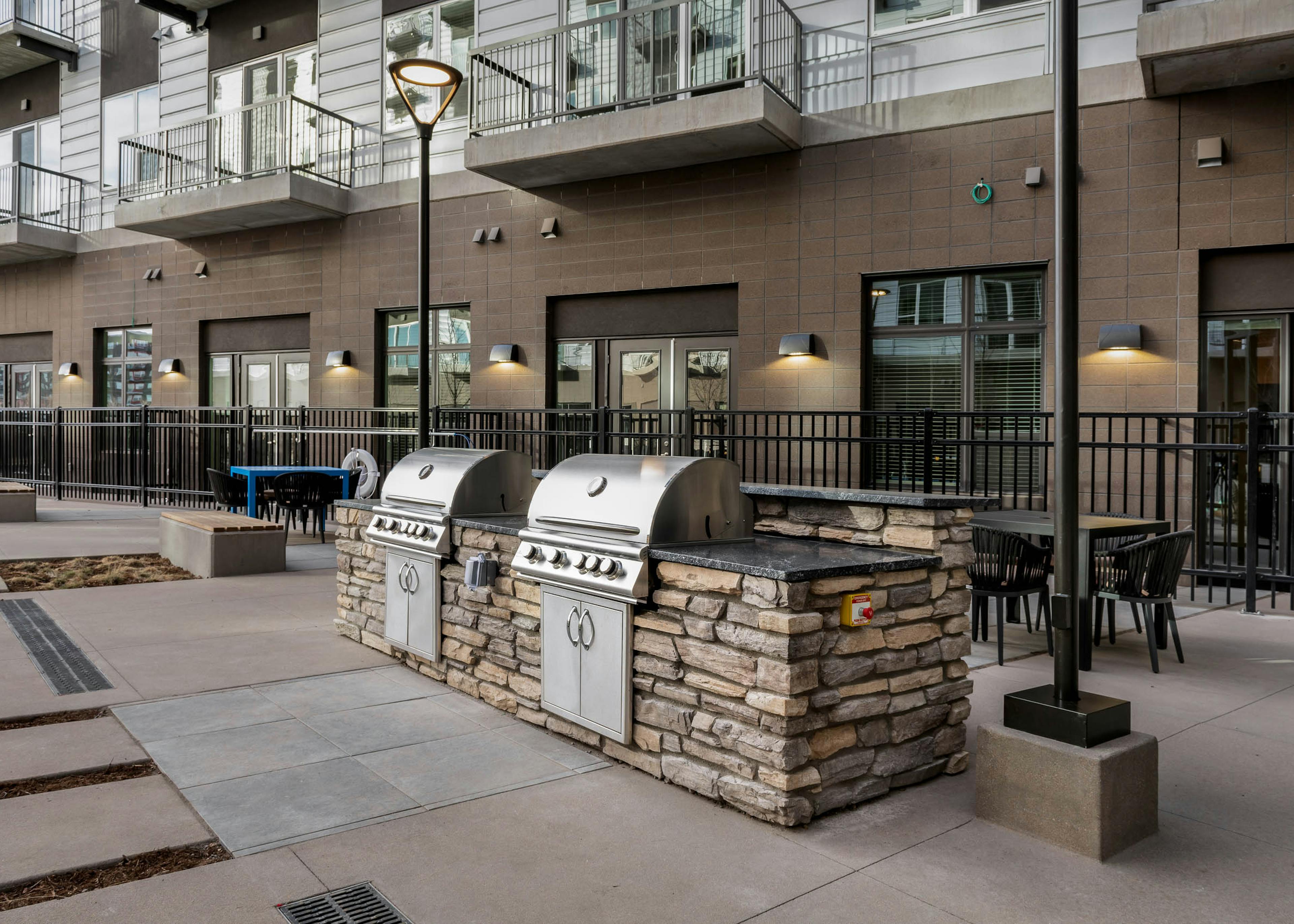 Exterior view of a grilling area at AMLI Art District with multiple tables with chairs and benches and apartment balconies