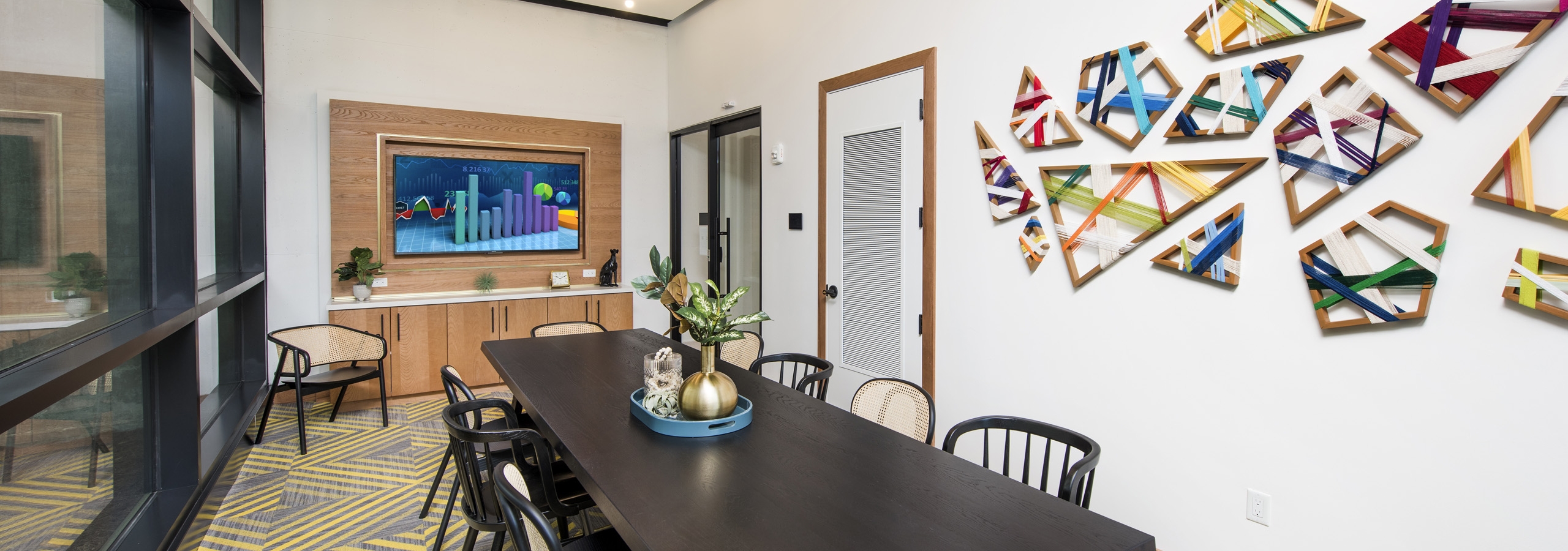 AMLI Lenox conference room with long dark table with 10 chairs and colorful wall art and large screen TV for presentations
