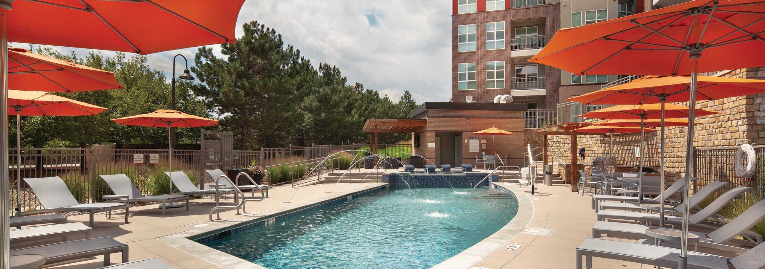 Exterior view of the pool at AMLI Dry Creek apartments with multiple seating areas and apartment balconies in the background