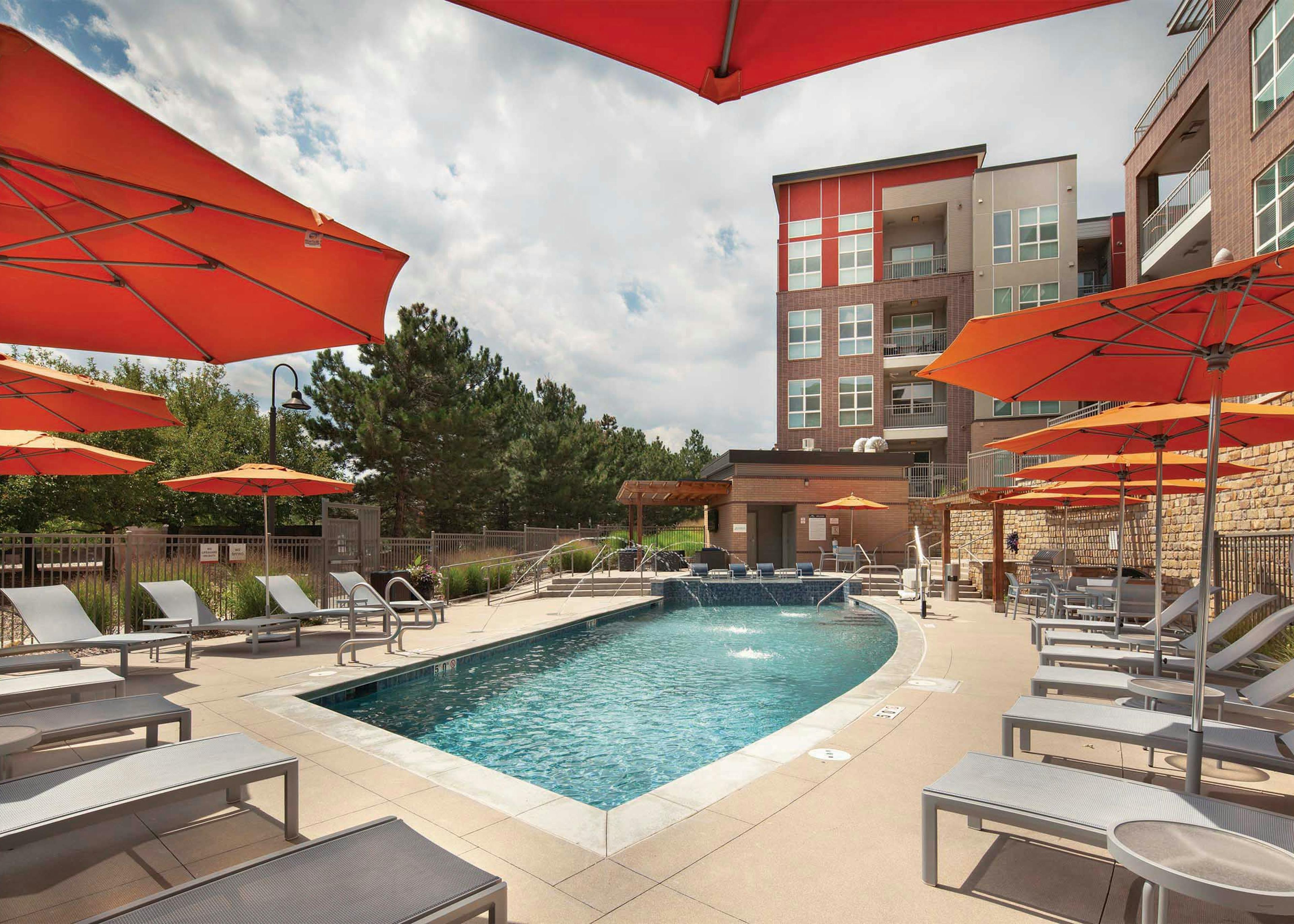 Exterior view of the pool at AMLI Dry Creek apartments with multiple seating areas and apartment balconies in the background
