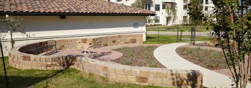 Paw park at AMLI on Riverside with a paved walking path and green grass with short brick ledges and a small dog walking