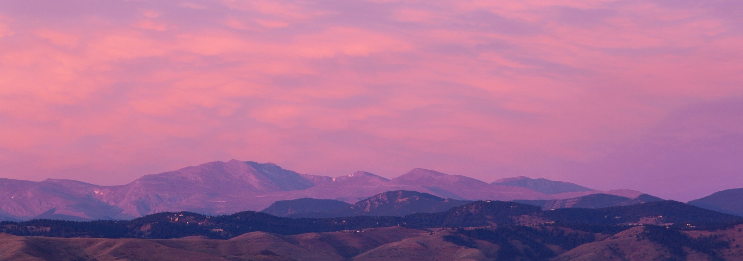 Mountain view from rooftop deck at AMLI Riverfront Green with rolling peaks with several clouds and purple and orange sky