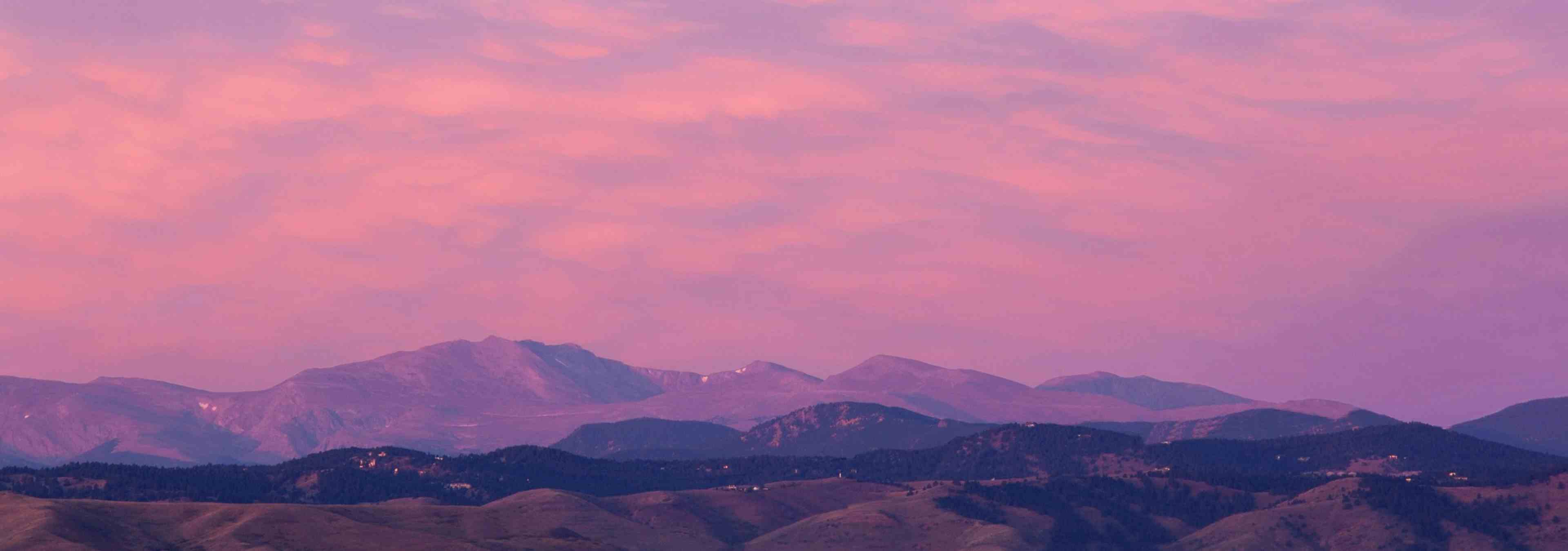 Mountain view from rooftop deck at AMLI Riverfront Green with rolling peaks with several clouds and purple and orange sky