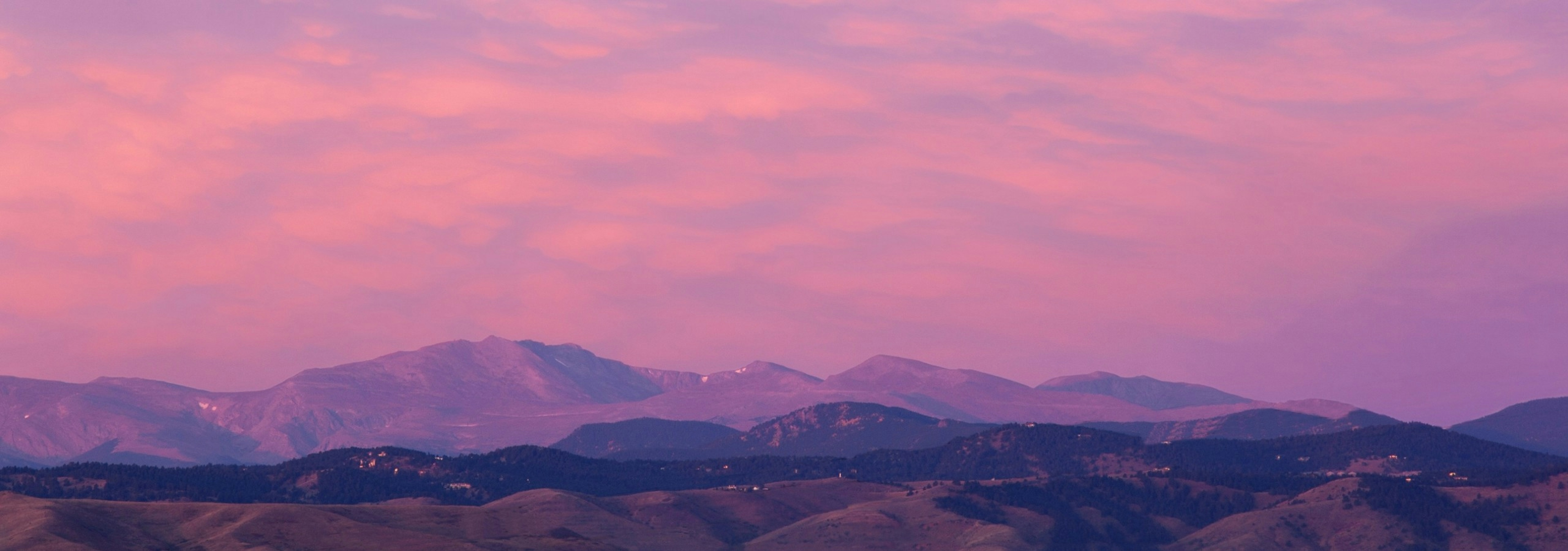 Mountain view from rooftop deck at AMLI Riverfront Green with rolling peaks with several clouds and purple and orange sky