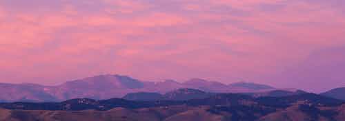 Mountain view from rooftop deck at AMLI Riverfront Green with rolling peaks with several clouds and purple and orange sky