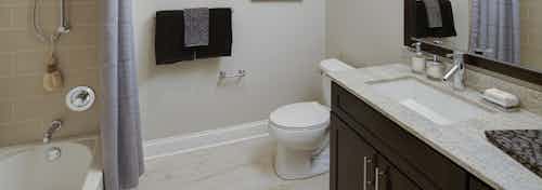 AMLI River North bathroom with a dark wood vanity near a toilet as well as a combined shower and tub with beige wall tiles