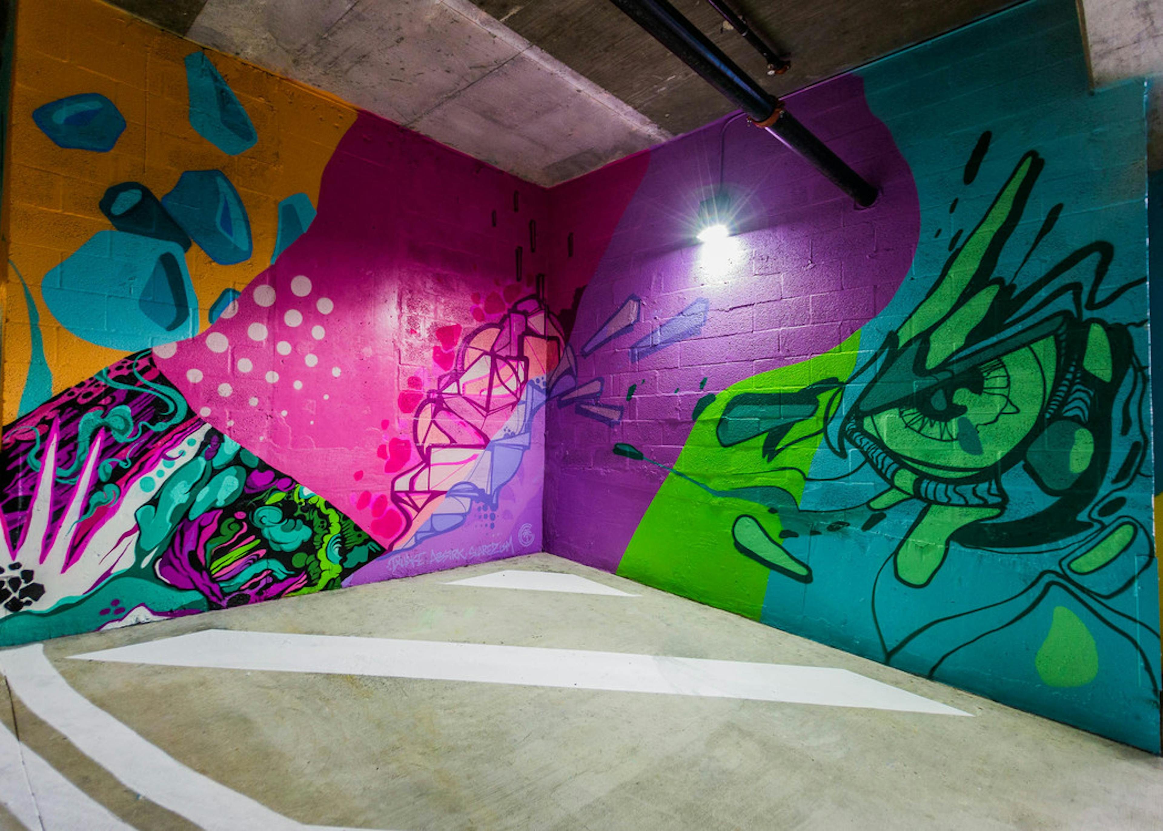 Interior of entrance to AMLI Dadeland apartments parking garage with colorful painted wall mural of palm leaf and many faces