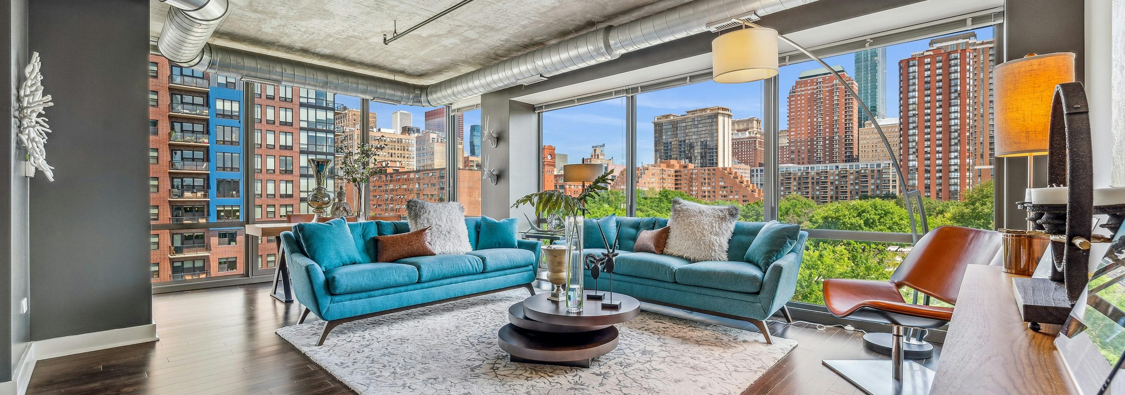 AMLI 900 living room with floor to ceiling view of city and blue couches with dark wood floors and distressed ceilings