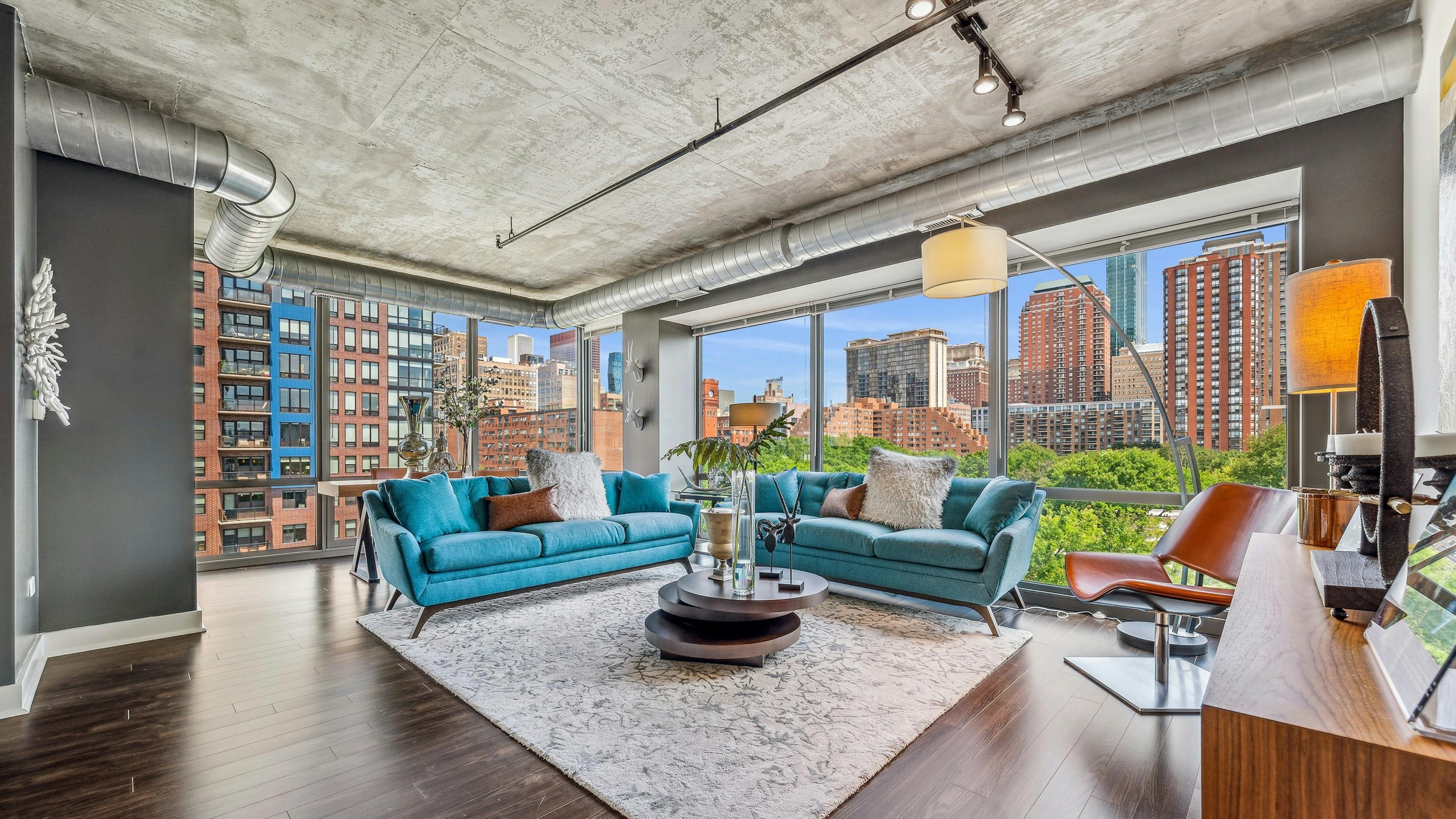 AMLI 900 living room with floor to ceiling view of city and blue couches with dark wood floors and distressed ceilings