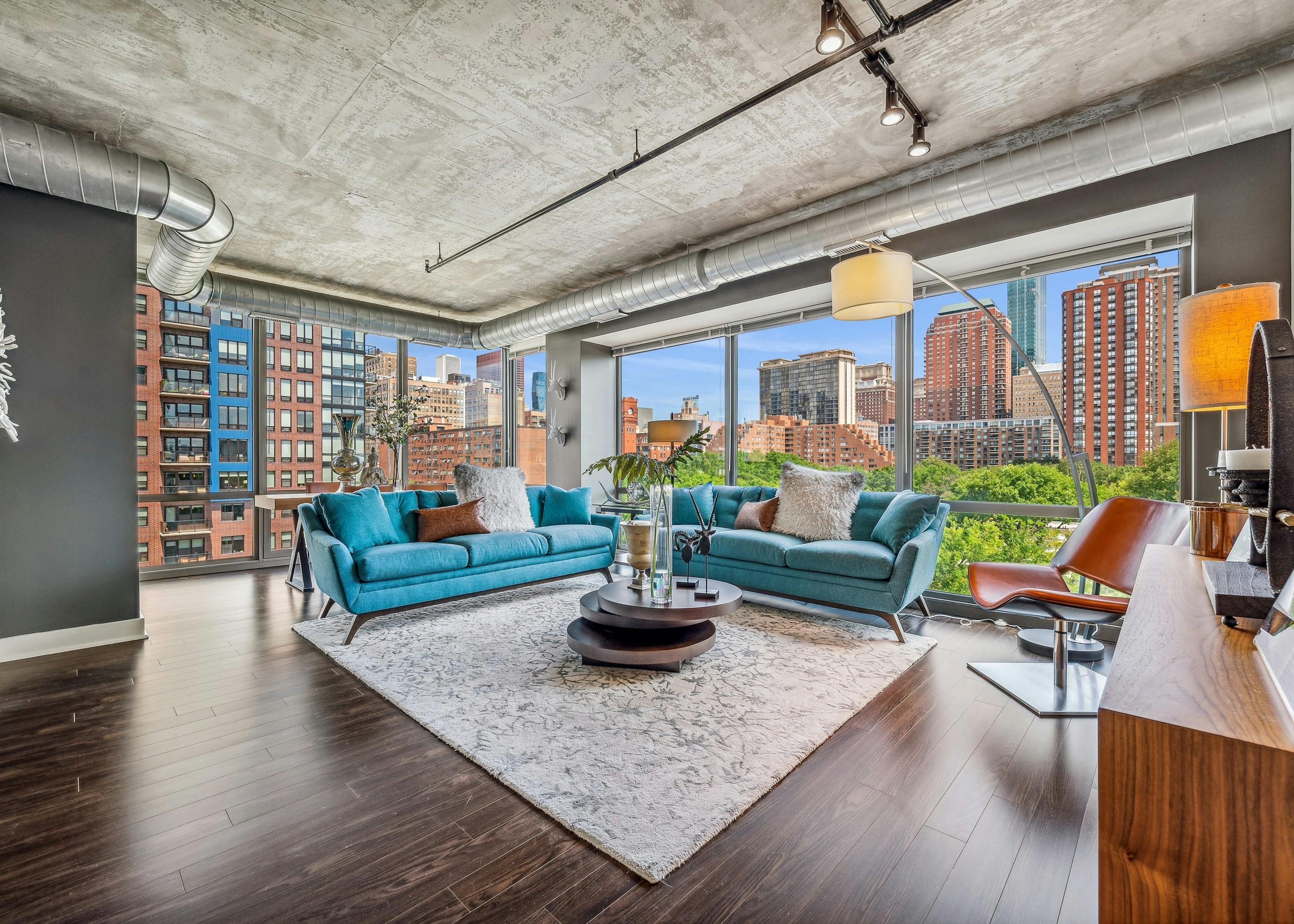 AMLI 900 living room with floor to ceiling view of city and blue couches with dark wood floors and distressed ceilings