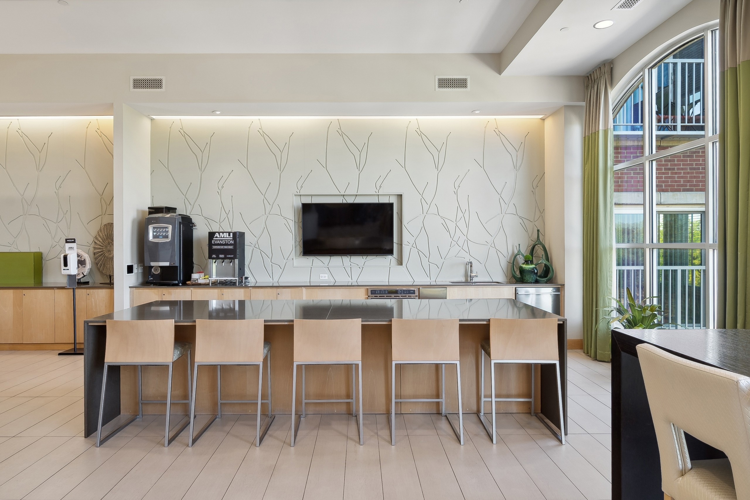 AMLI Evanston resident lounge with coffee bar and large counter and five beige stools facing TV on beige wall