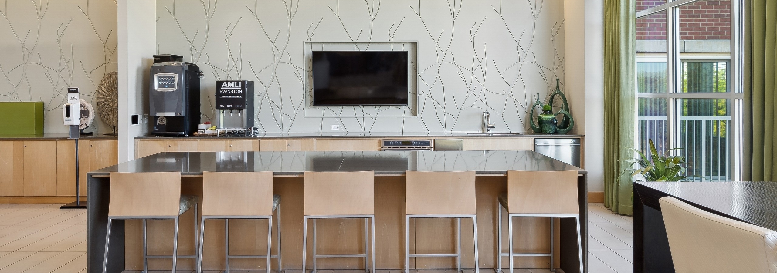 AMLI Evanston resident lounge with coffee bar and large counter and five beige stools facing TV on beige wall