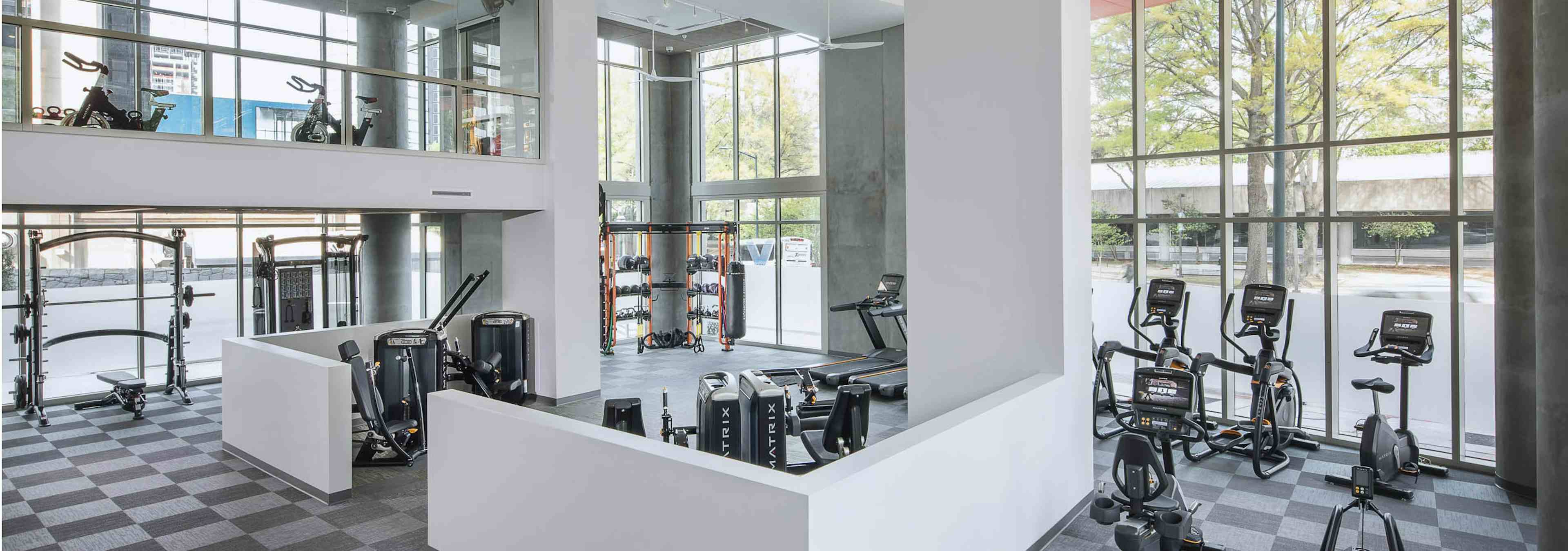 AMLI Arts Center fitness center with checkered flooring and a variety of exercise machines facing floor to ceiling windows