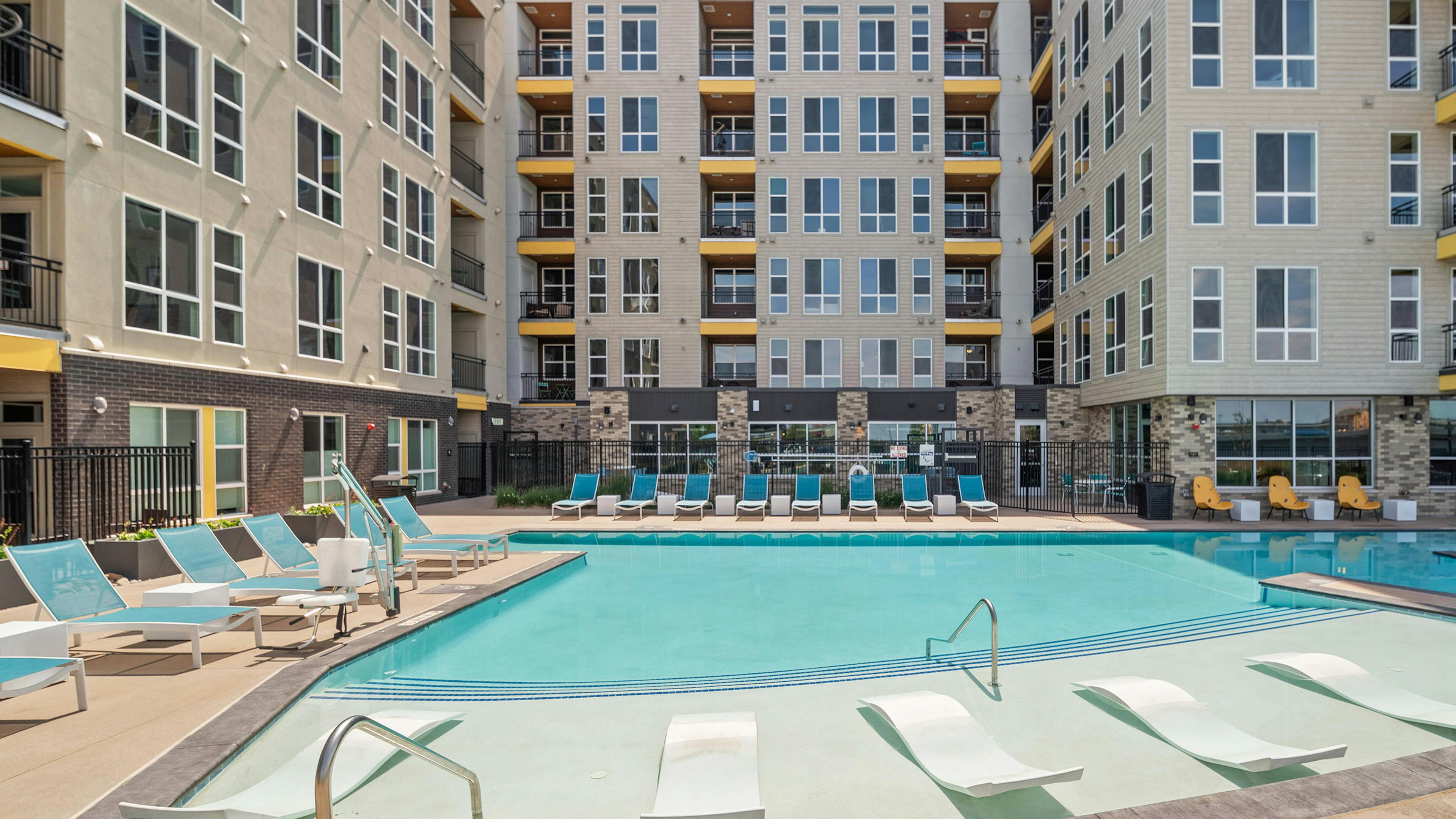 Courtyard pool with lounge seating inside and outside of water surrounded by AMLI RiNo beige and brown building 