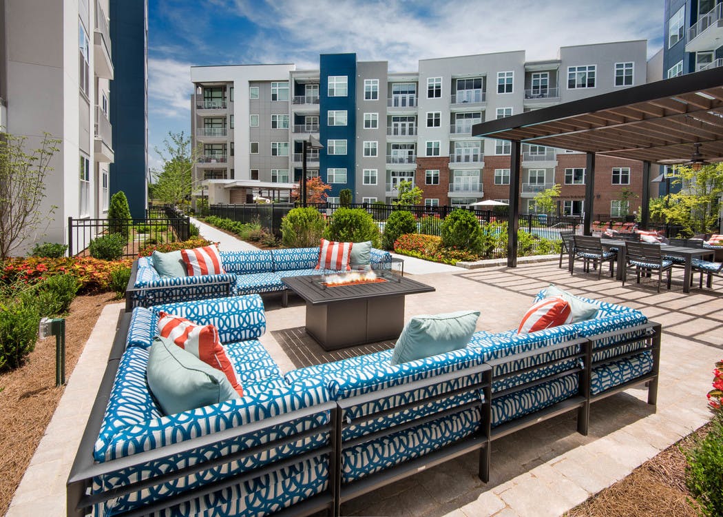 Two patterned blue L couches with a fire pit in the center and green foliage surrounding the patio area at AMLI Buckhead