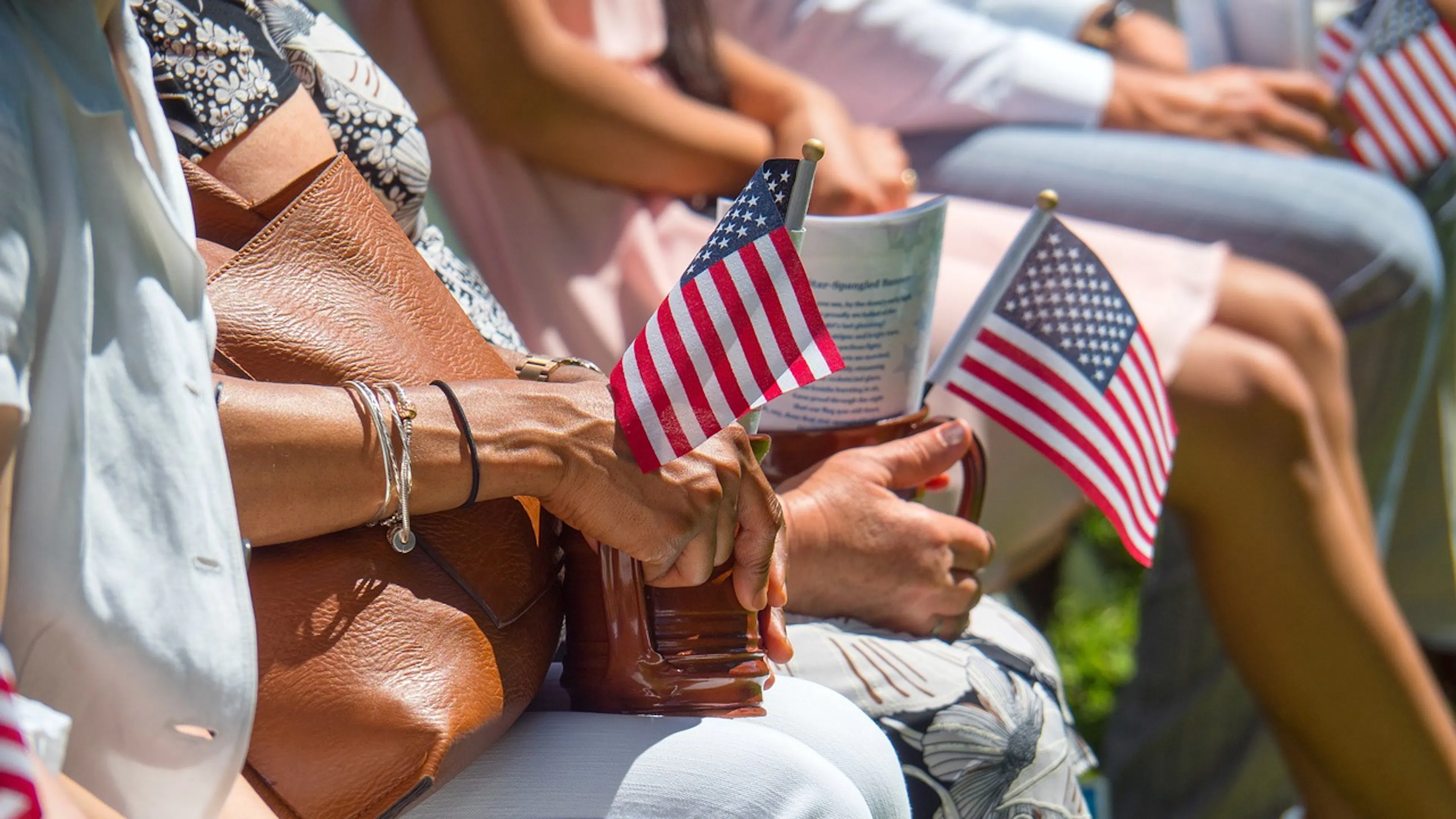 A row of people sitting on lawn chairs holding mini American flags in their hands
