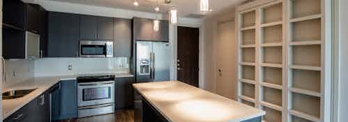 Interior of AMLI Design District apartment kitchen with dark brown cabinetry, wood floors and stainless steel appliances