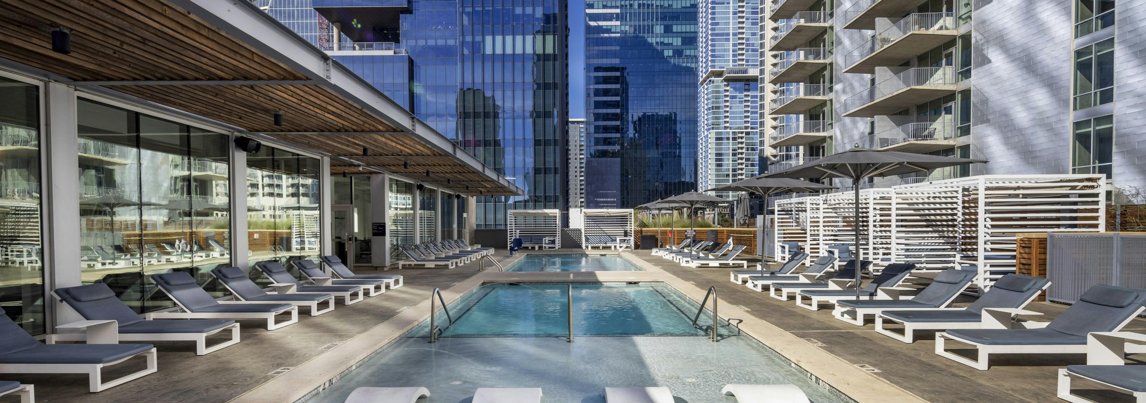 Close up view of sleek white lounge chairs in shallow portion of AMLI on 2nd rooftop pool surrounded by daytime city views