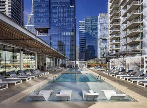 Close up view of sleek white lounge chairs in shallow portion of AMLI on 2nd rooftop pool surrounded by daytime city views