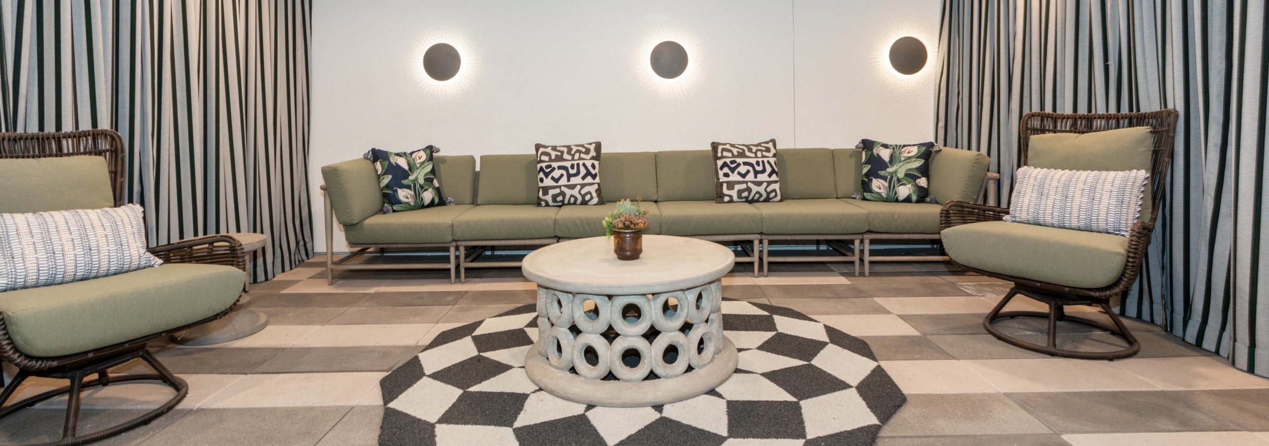 Daytime view of an outdoor courtyard hangout cave with long couch, striped curtains and checkered rug at AMLI Park Broadway