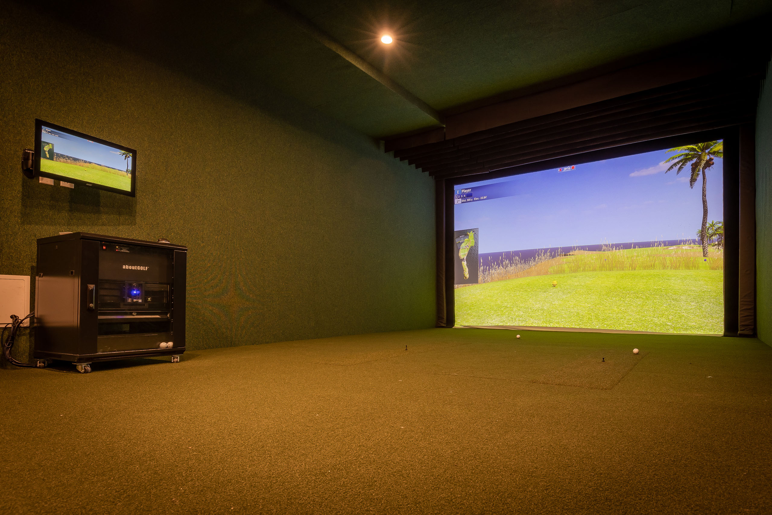 Golf simulator at AMLI Midtown Miami apartments with turf with 2 golf balls and a large screen showing grass and golf balls