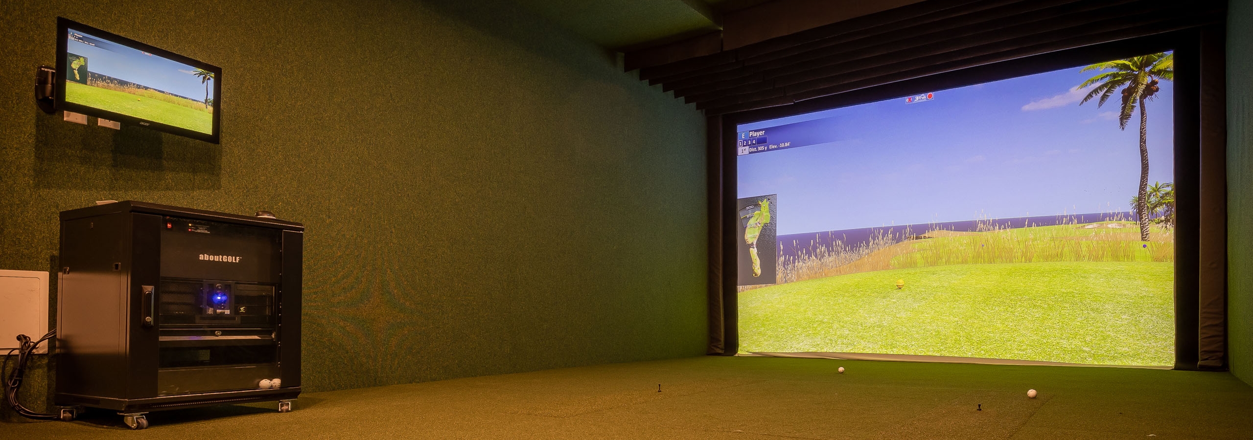 Golf simulator at AMLI Midtown Miami apartments with turf with 2 golf balls and a large screen showing grass and golf balls