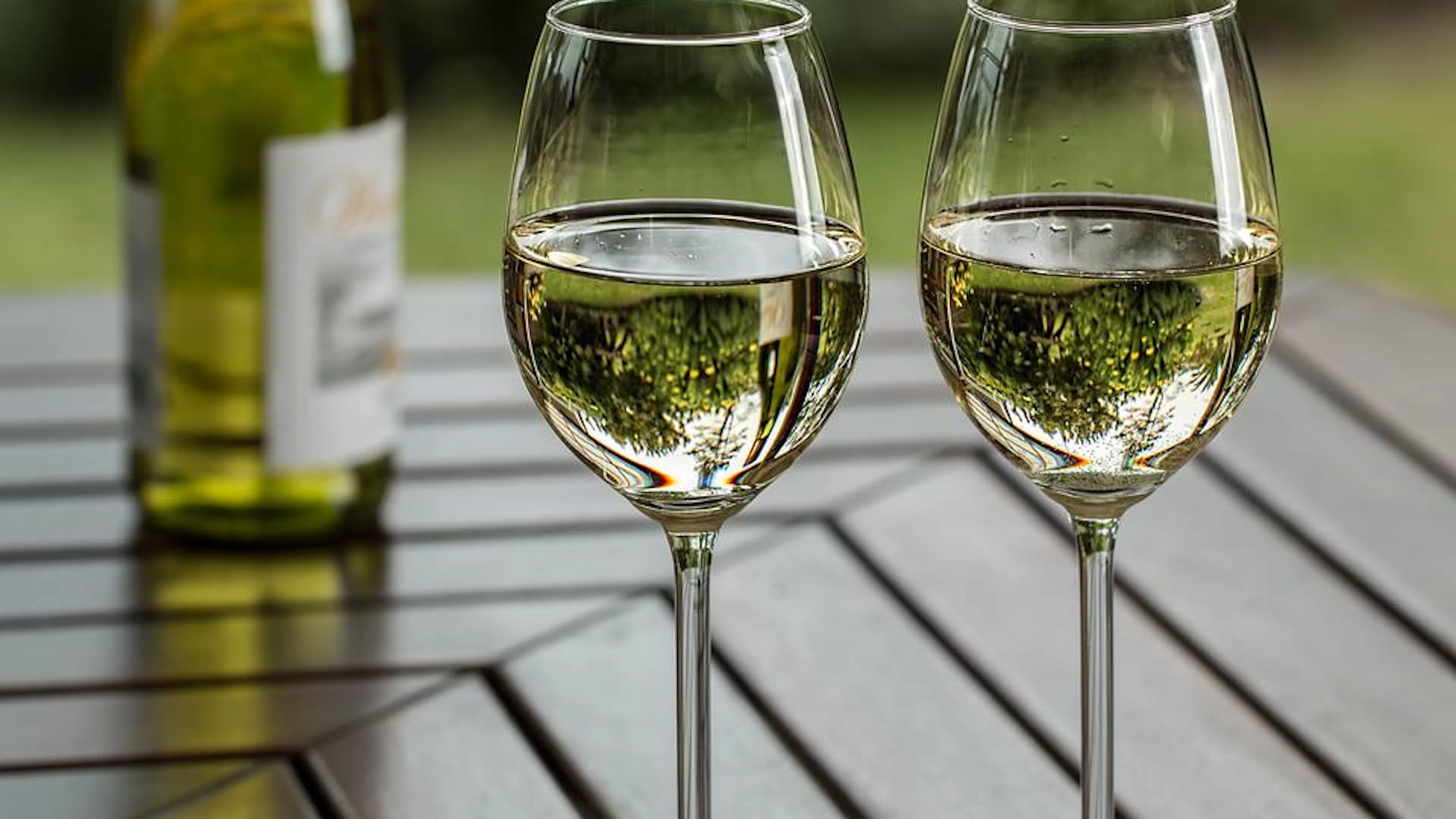 Two white wine glasses filled with wine on a wooden table