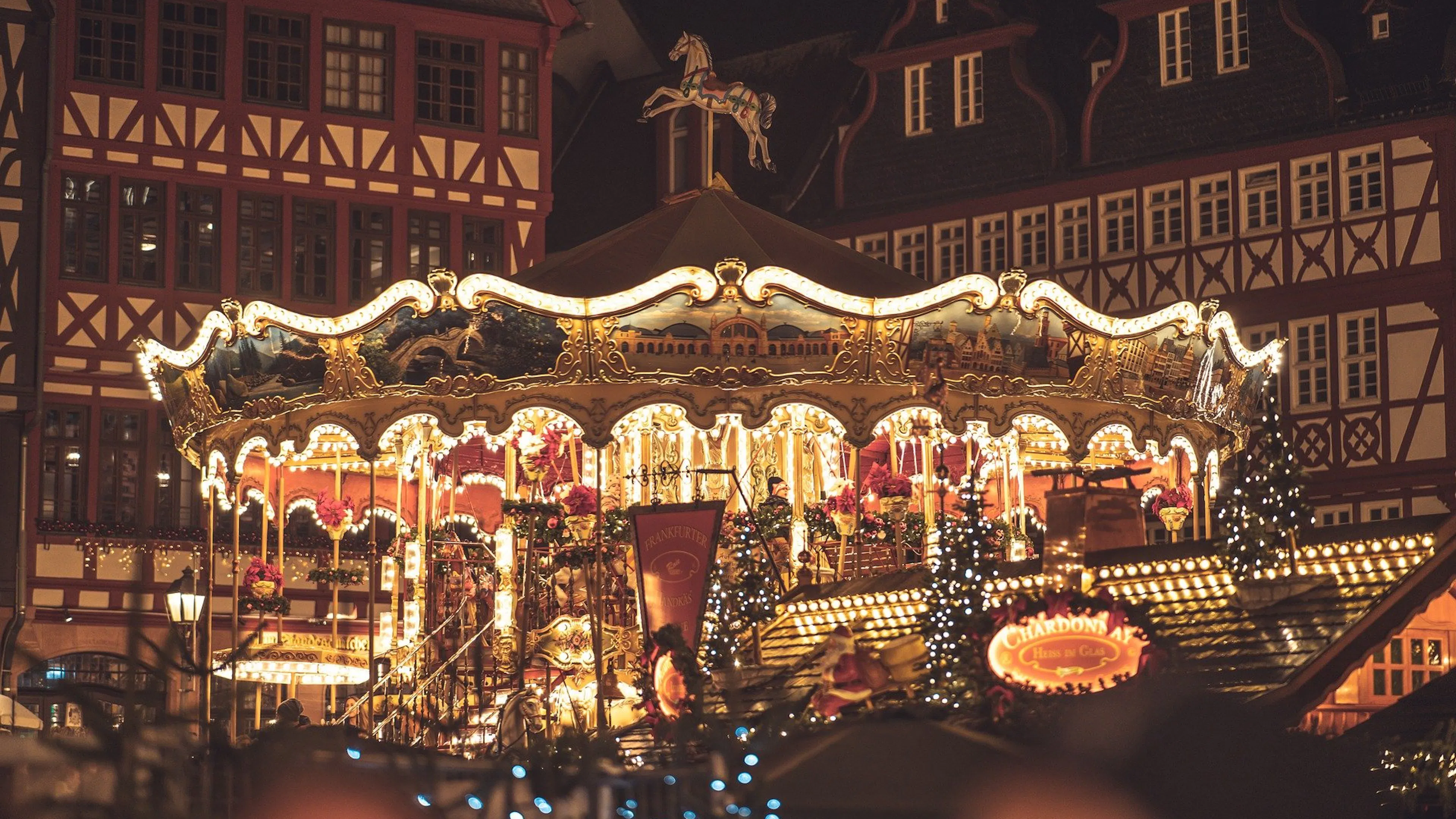 A grand carousel lit with Christmas lights and intricately painted in a town square surrounded by Bavarian style buildings