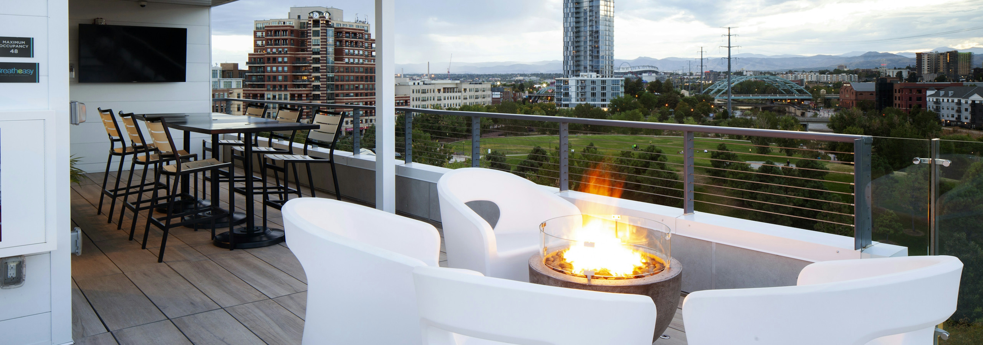 An exterior view of AMLI Riverfront Green roof top deck with fire pit and furniture and mountain view and sky scraper views