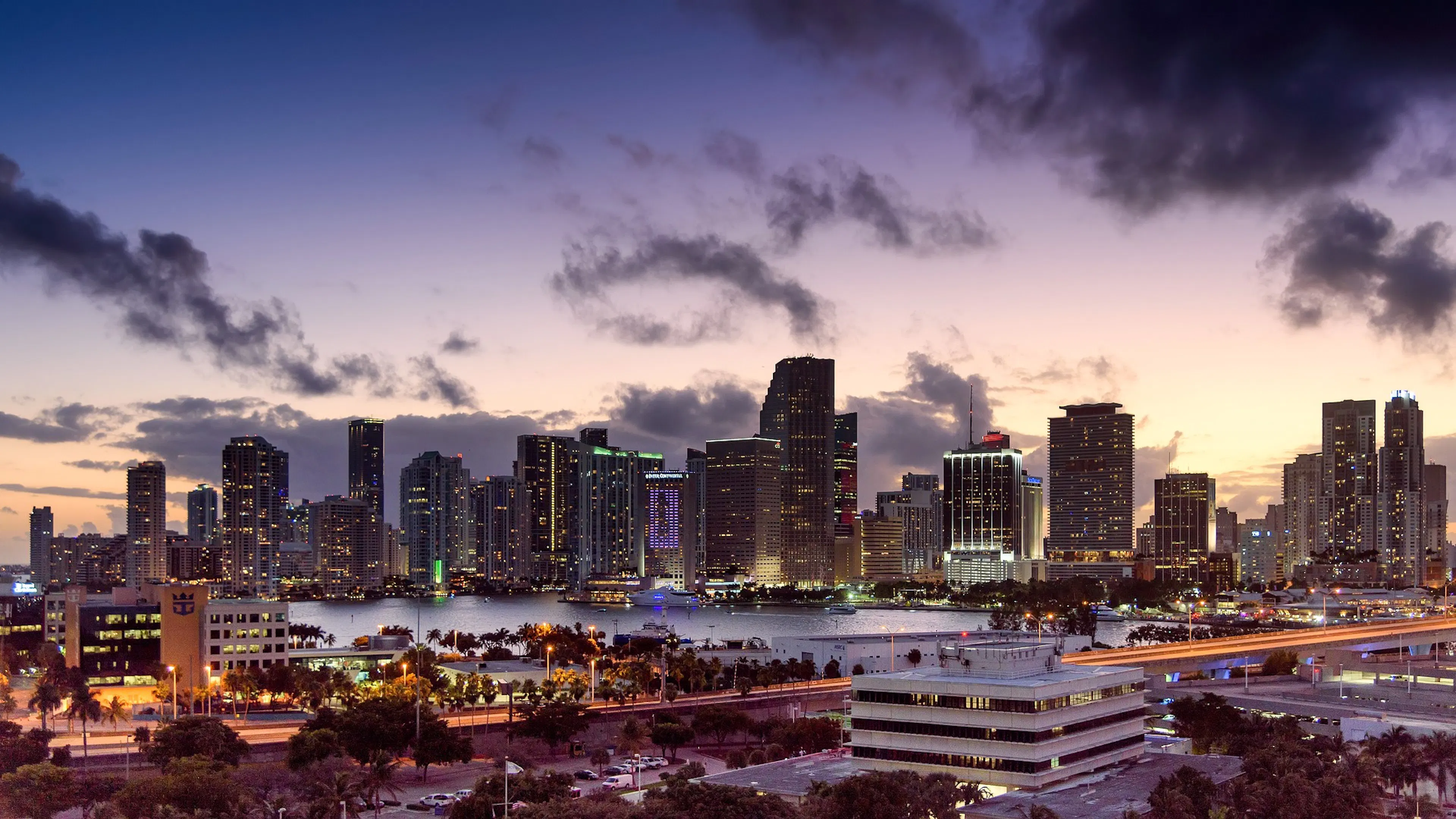 A long exposure wide view of Miami’s skyline at night with streaks of bright light from the highway in the foreground