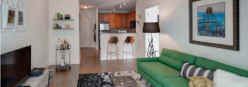 An AMLI 900 apartment living room with wood flooring connecting to a kitchen with granite countertops and bar stools
