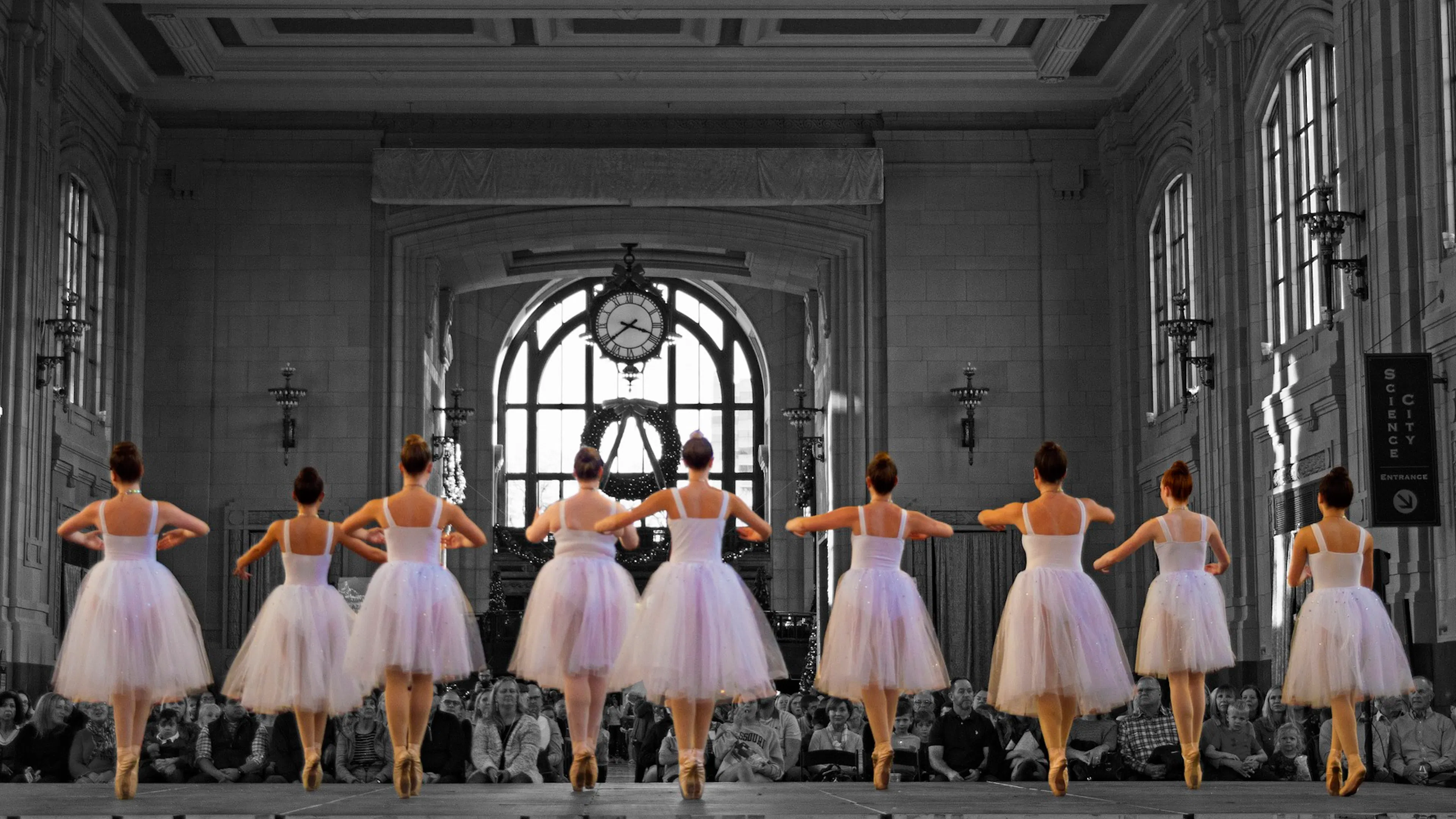 ballerinas in a row with pink dresses on stage with a black and white audience in church