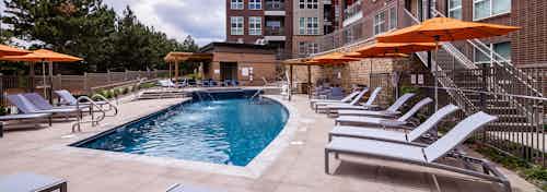 Daytime view of the pool at AMLI Dry Creek apartments with lounge chairs and orange umbrellas and view of apartments windows