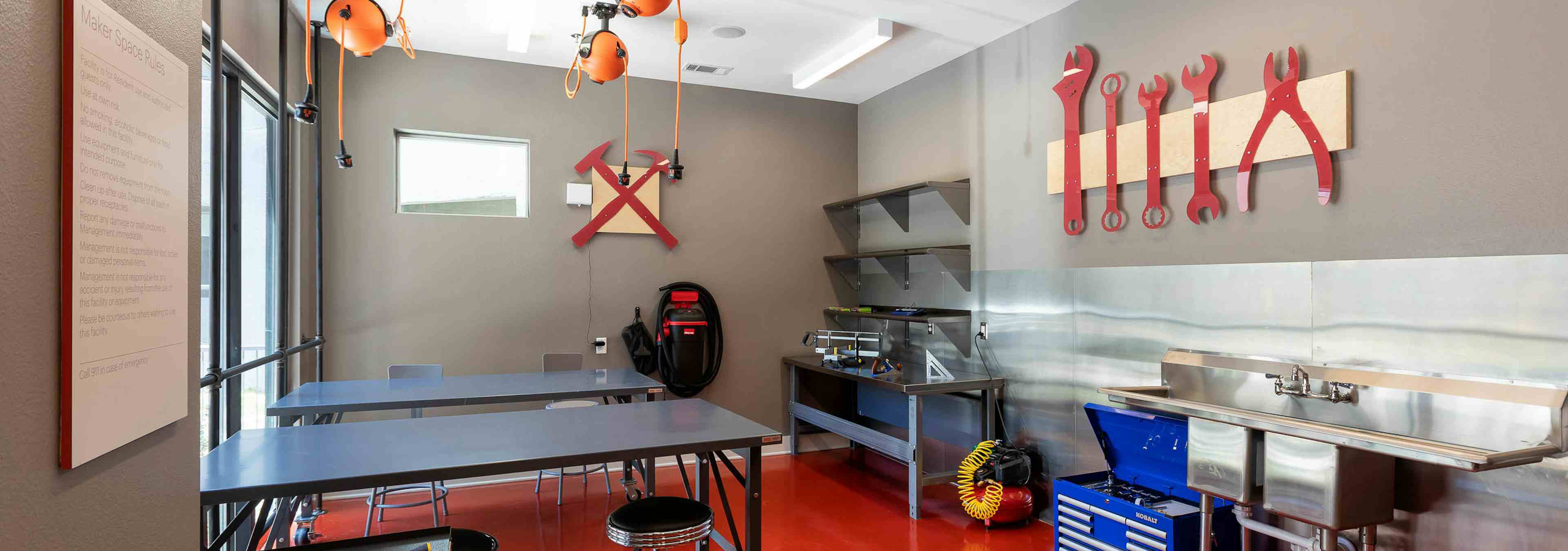 Makers space at AMLI on Aldrich with grey table and chairs and different stations with red tools on walls for creating