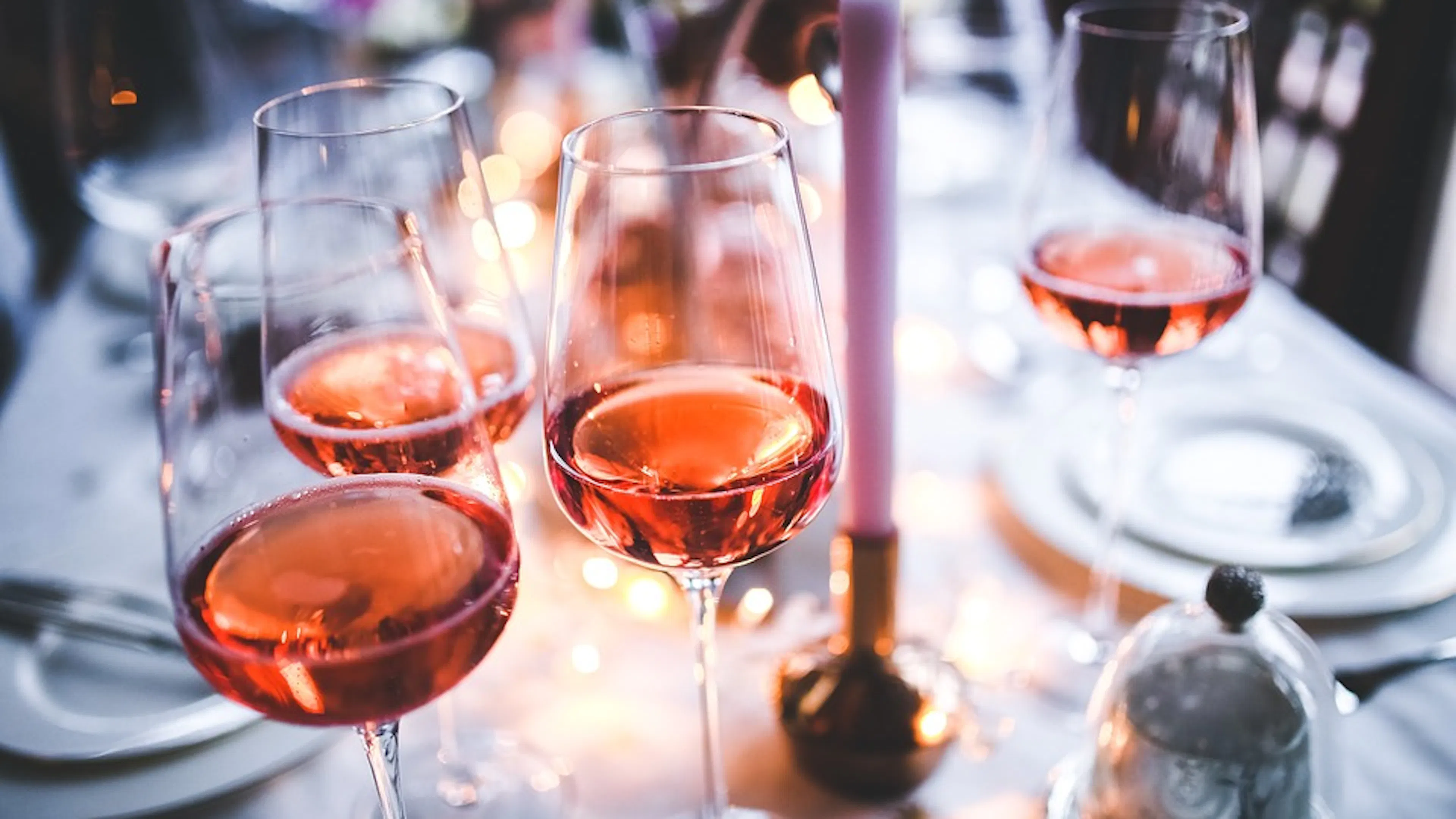 Delicate glasses of wine on a set table beside stacked plates and lit candles