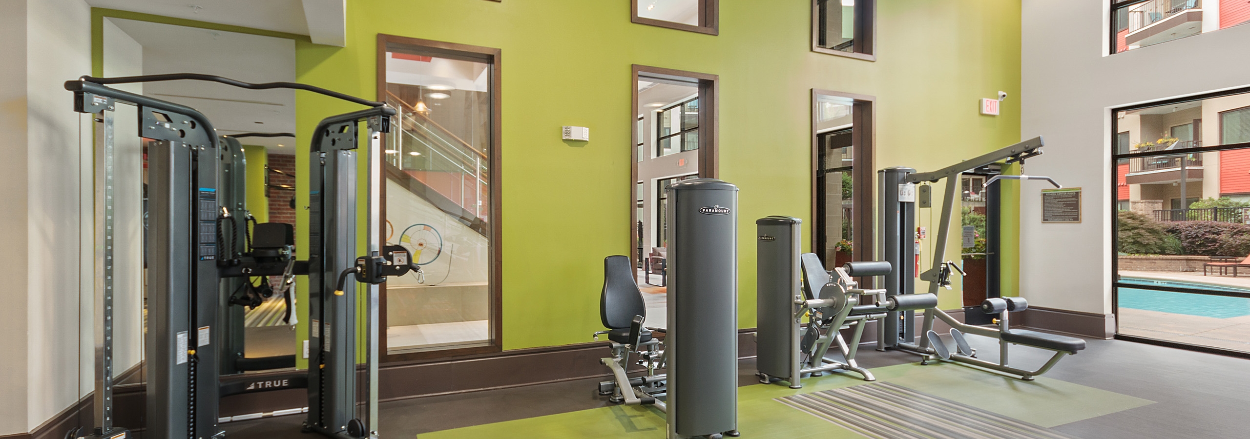 Interior of the fitness center at AMLI Ponce Park apartments with multiple weight machines and bright green two story wall