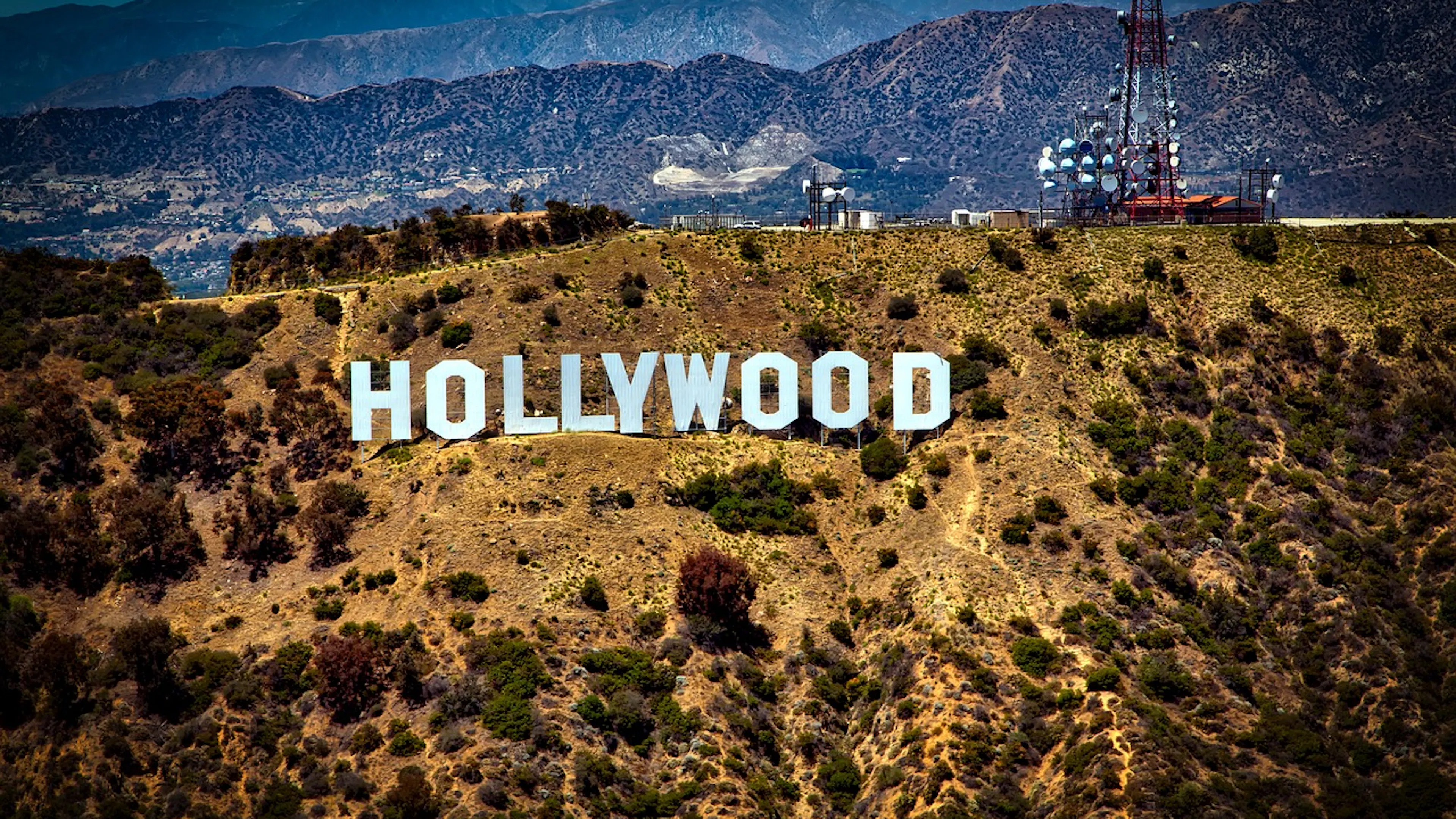 The Hollywood sign on a hill covered in shrubs with the city far off in the distance