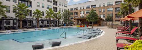 Daytime view of AMLI on Aldrich courtyard pool with gray lounges in water and surrounding cabanas and lounges and palm trees
