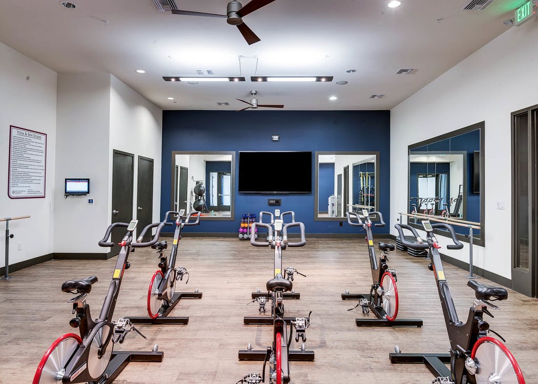 A spin studio at AMLI Cherry Creek apartments with multiple stationary bikes and a large television and hard wood floors