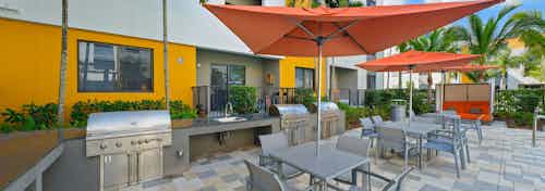 One of two barbeque areas at AMLI 8800 with electric grilling stations, outdoor tables with orange umbrellas and palm trees