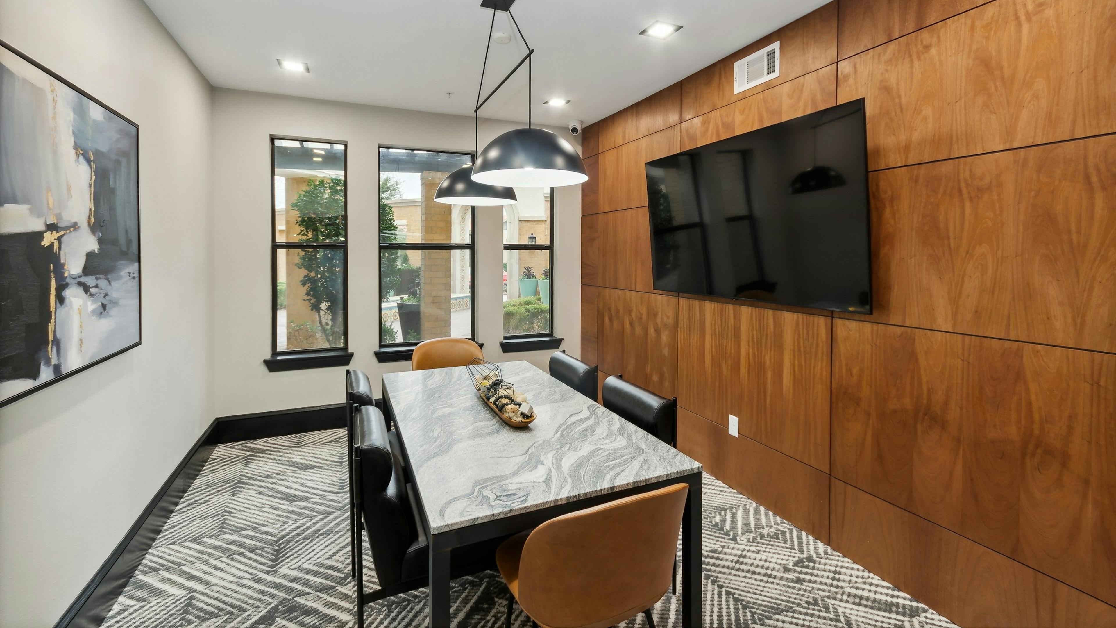 Conference room at AMLI Campion Trail apartments with gray stone table and six chairs and big screen TV on wood paneled wall