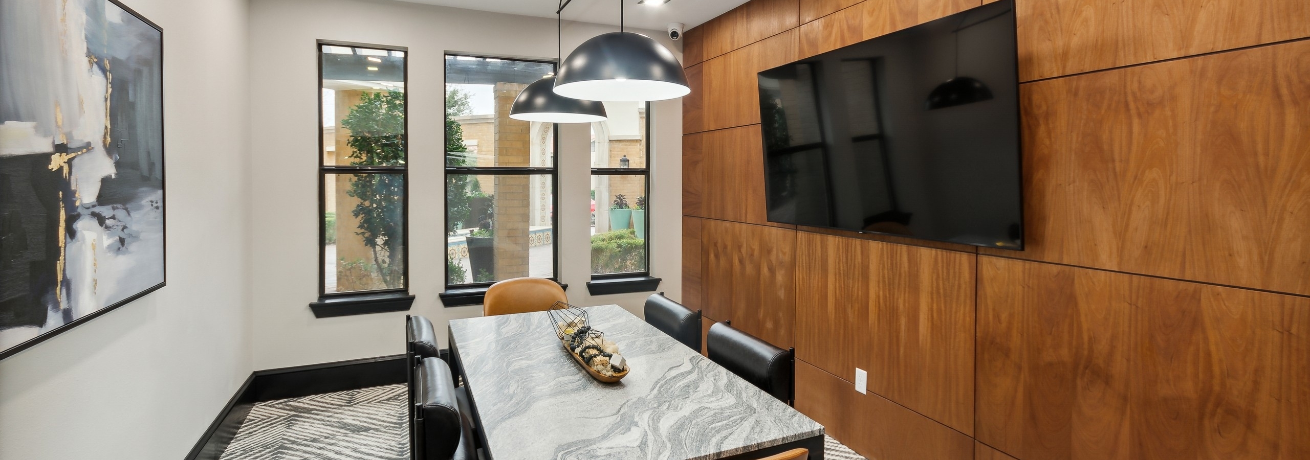 Conference room at AMLI Campion Trail apartments with gray stone table and six chairs and big screen TV on wood paneled wall