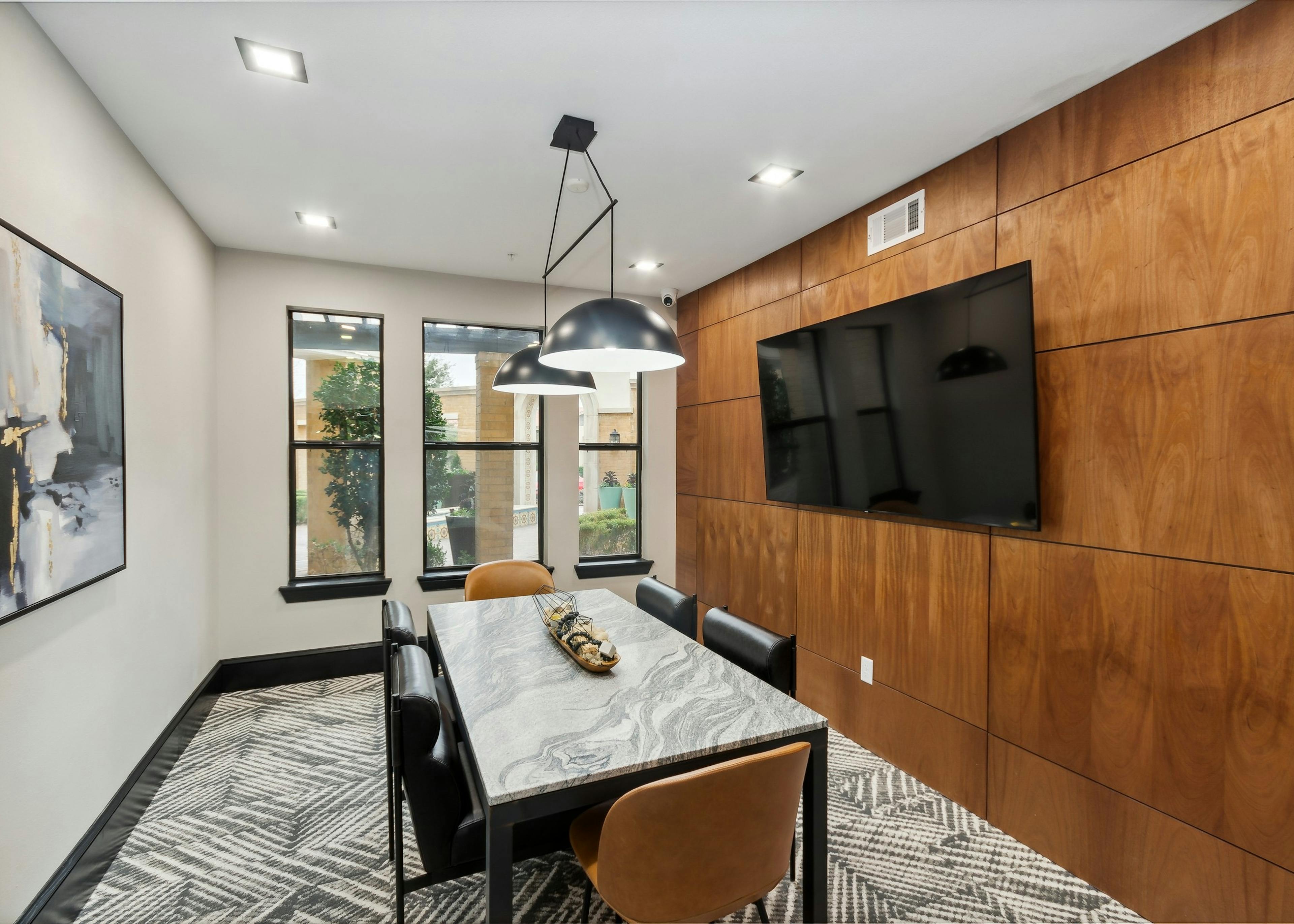 Conference room at AMLI Campion Trail apartments with gray stone table and six chairs and big screen TV on wood paneled wall