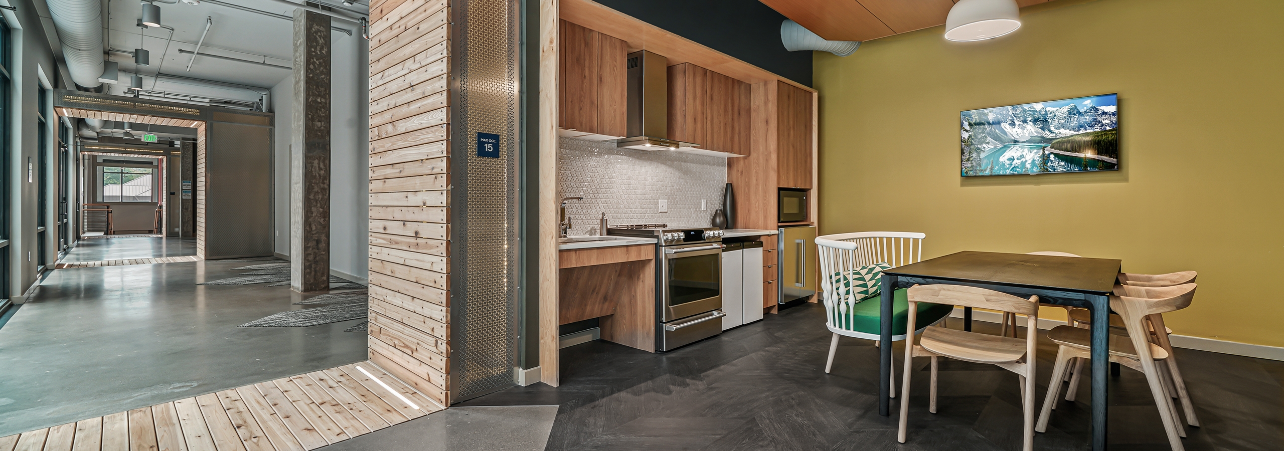 AMLI Spring District kitchen lab with stove and microwave and table and chairs and mounted TV and wide hallway at left