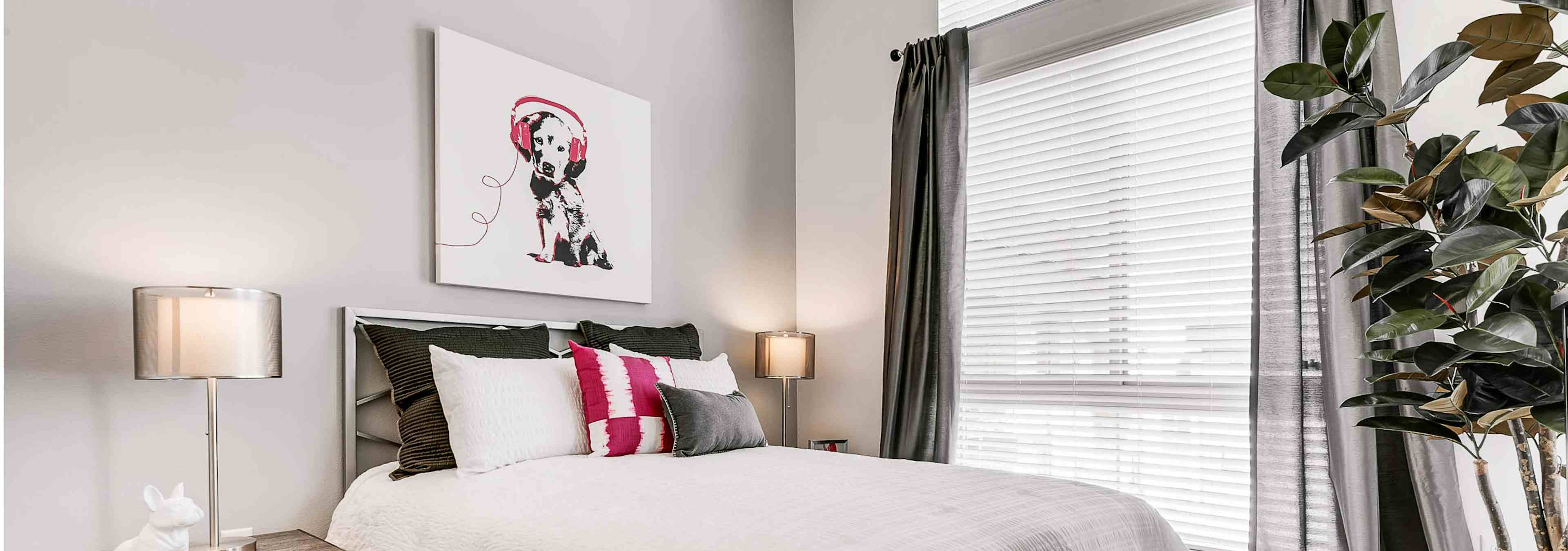 Interior view of a bedroom at AMLI Cherry Creek apartments with white linen and walls with lamps and a plant and window view