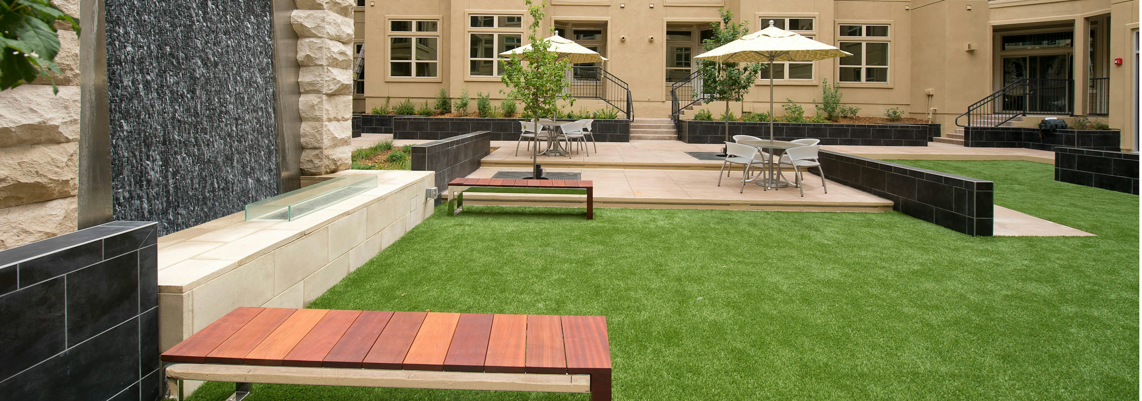 Daytime view of AMLI RidgeGate Zen garden with cascading stone waterfall, turf and various seating with umbrellas and trees