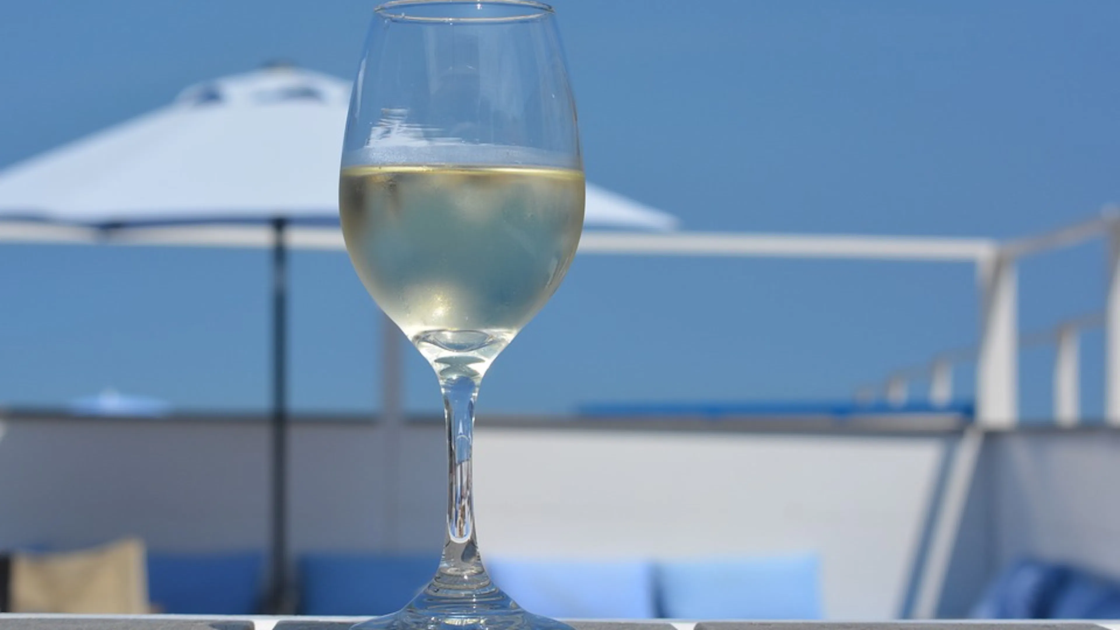 A glass of chilled white wine on an outdoor table with the ocean in the background