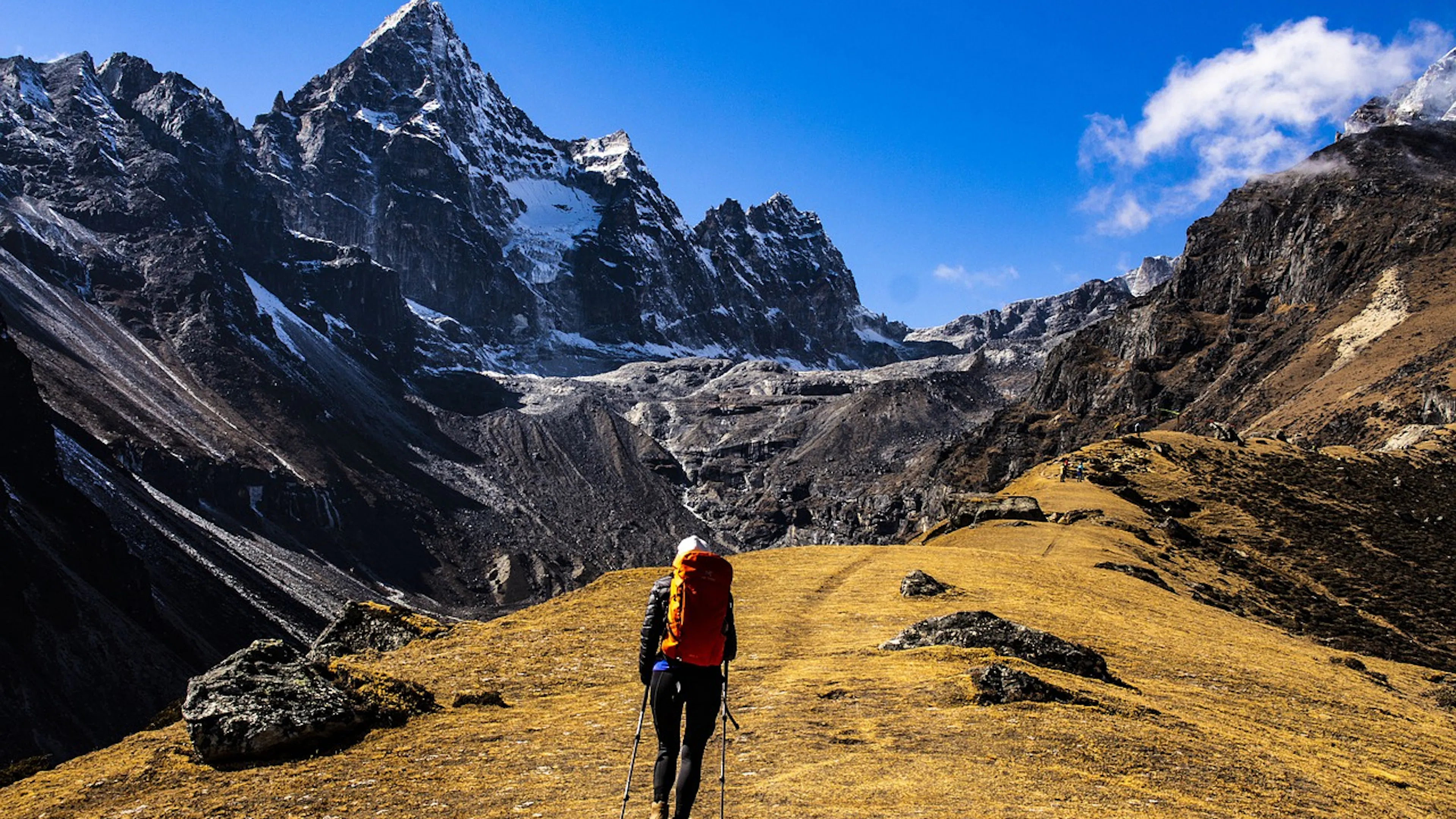 A person hiking on a grassy trail toward a tall mountain range