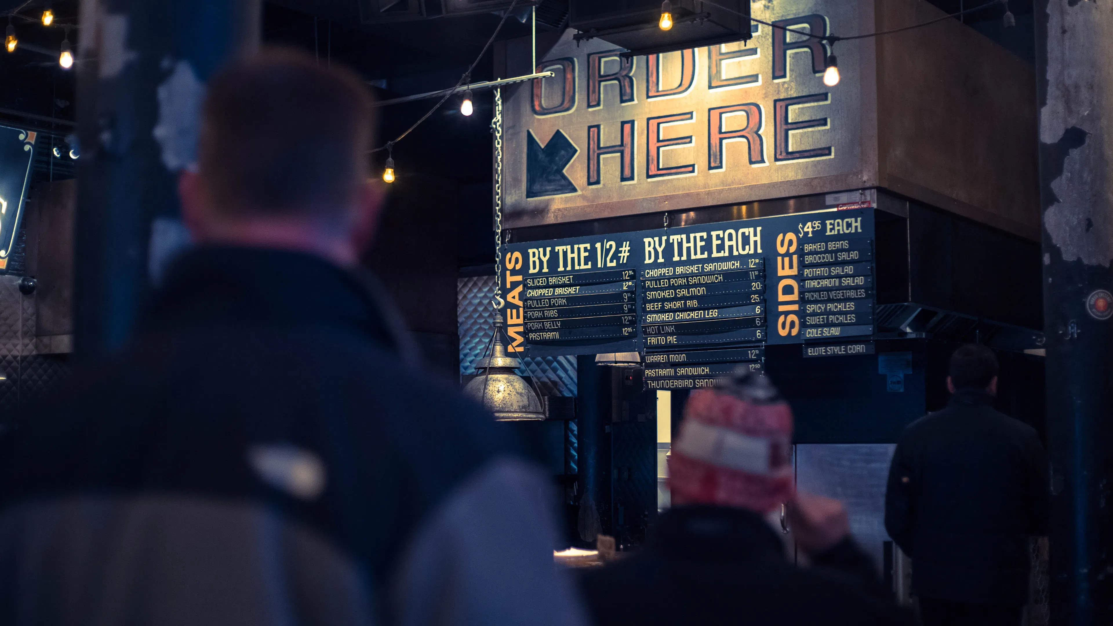 A man looking away from the camera at a menu board in a dark restaurant